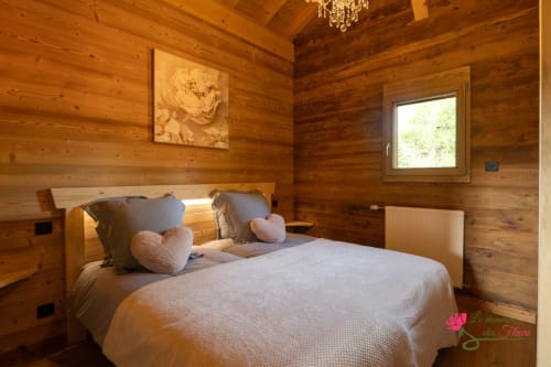 Chambre cosy en bois au Domaine des Fleurs avec lit queen, coussins cœur rose et vue montagne à Gérardmer
