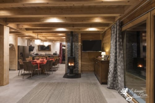 Intérieur spacieux du chalet Le Domaine des Fleurs à Gérardmer avec poutres apparentes, salle à manger, cheminée et décor moderne