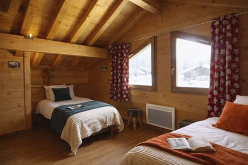 Chambre chaleureuse du chalet avec lits jumeaux, rideaux à fleurs rouges et vue sur les montagnes au Domaine des Fleurs, Gérardmer
