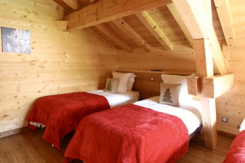Chambre cosy du chalet en bois avec deux lits, couvertures rouges et poutres apparentes au Domaine des Fleurs, Gérardmer