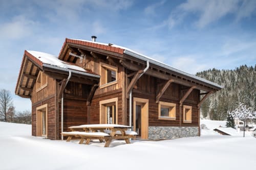 Chalet en bois moderne à Gérardmer enneigé avec vue sur les montagnes, tables de pique-nique sur terrasse et soubassement en pierre