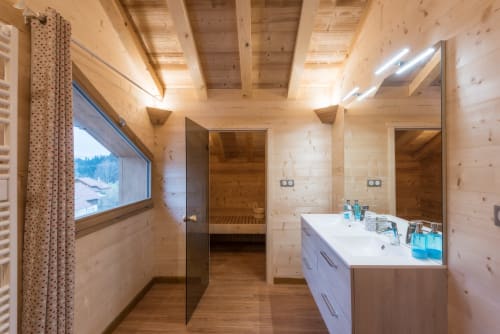Salle de bain spacieuse du chalet La Reine des Prés avec fixtures en bois, double vasque, accès au sauna et vue montagne