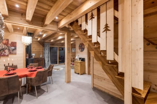Salle à manger du Chalet La Reine des Prés avec poutres apparentes, table rouge et escalier au Domaine des Fleurs, Gérardmer