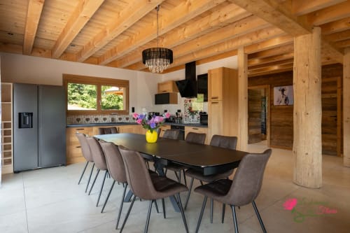 Salle à manger chalet moderne avec poutres en bois, table noire, chaises grises et cuisine, Le Domaine des Fleurs