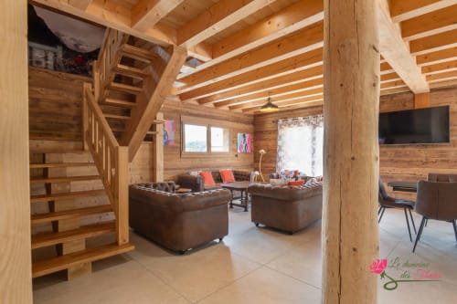 Spacieux salon de chalet en bois avec sièges en cuir, poutres apparentes, escalier et vue sur les montagnes au Domaine des