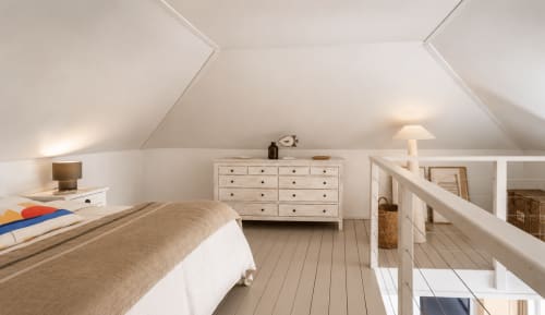 Chambre lumineuse sous les combles du bungalow de Saint-Martin avec murs blancs, parquet, lit, commode et vue sur mer