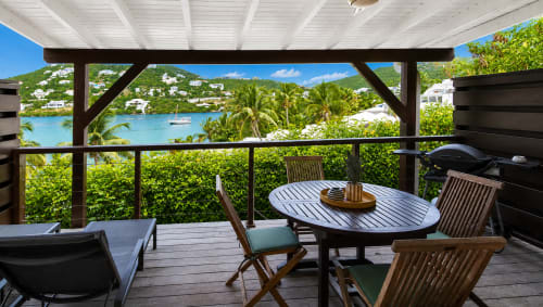 Terrasse de bungalow surplombant la baie d'Oyster Pond, Saint-Martin, avec table à manger, chaises longues et vues sur le jardin tropical