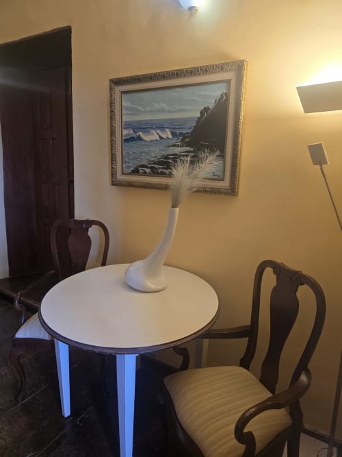 Elegante comedor en suite del Hotel Rural la Raya 1866 con mesa redonda, sillas de madera y cuadro de paisaje costero