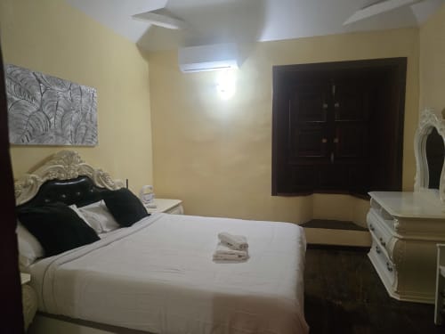 Elegante suite de dormitorio en Hotel Rural la Raya 1866 en Tenerife con cama blanca, cabecero ornamentado y paredes color crema