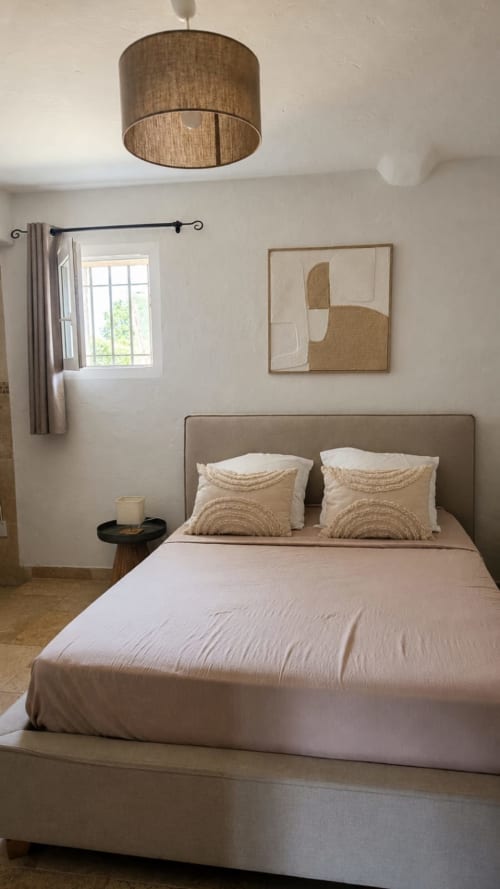 Chambre douillette au Mas Manon B&B à Cavaillon avec luminaire texturé, literie beige et art mural abstrait