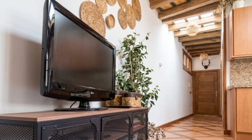 Sala de estar del apartamento Cerezo en El Aserradero con televisor de pantalla plana, vigas de madera, decoración tejida en pared y planta en maceta en La