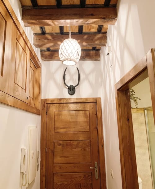 Pasillo rústico en El Aserradero con vigas de madera, paredes blancas, lámpara tejida y decoración con cuernos oscuros
