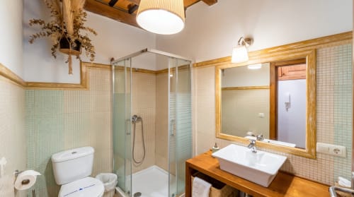 Baño moderno en el apartamento Cerezo del hotel El Aserradero, La Alberca, con ducha de cristal, tocador de madera y azulejos verde menta