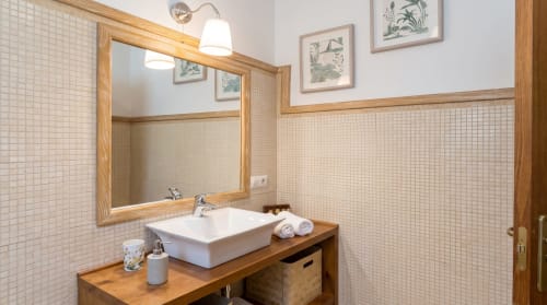 Baño moderno en apartamento Cerezo de El Aserradero, La Alberca, con lavamanos de cerámica blanca, tocador de madera y paredes revestidas en azulejos crema