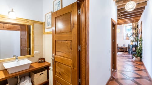 Baño de madera con lavabo, espejo y puerta que accede al pasillo en apartamento Cerezo de El Aserradero, La Alberca