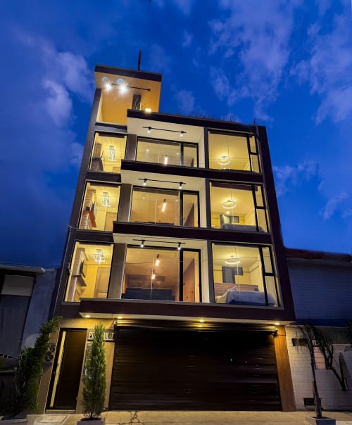 Edificio hotelero de 4 pisos iluminado al anochecer en Las Vigas de Ramírez, México, con amplios ventanales y entrada de garaje