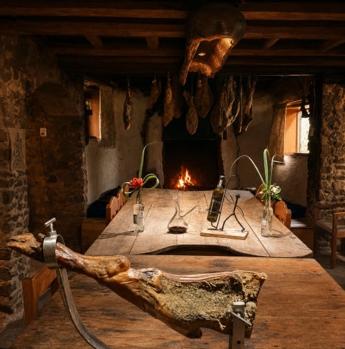 Comedor rústico de piedra en hotel Sento SanMa con chimenea, vigas de madera y carnes curadas colgantes en San Mateo Rio Hondo,