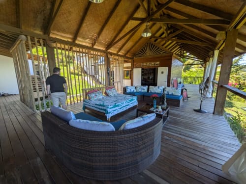 Vaste terrasse couverte en bois à Fare Tihi Moana à Tumaraa avec sièges lounge, coussins bleus et vue tropicale luxuriante