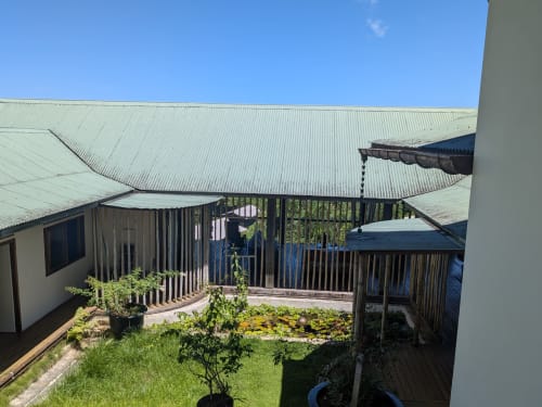Cour du bungalow Fare Tihi Moana à Tumaraa avec terrasse en bois, jardin et bâtiments aux toits métalliques sous un ciel bleu