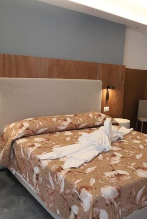 Camera moderna alle Totonno's Rooms di Tropea con testata color panna, biancheria a motivi e parete in legno