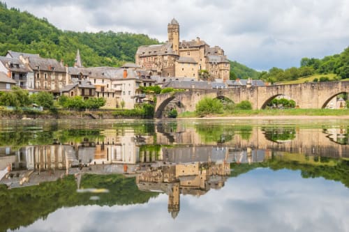 Château médiéval et pont de pierre reflétés dans l'eau calme de la rivière à Estaing, France
