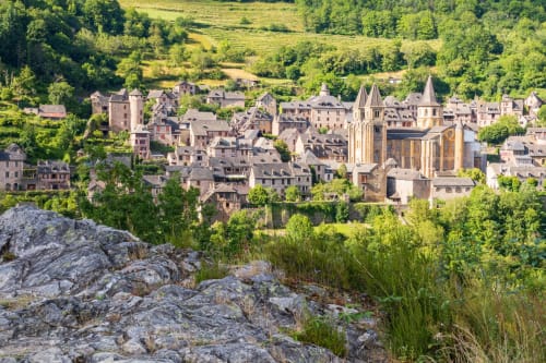 Le village d'Estaing niché dans la verdoyante campagne française avec ses bâtiments historiques en pierre et clochers d'église entourés de collines vertes