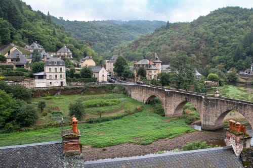 Pont de pierre traversant une rivière, village médiéval blotti dans une vallée boisée, Hôtel du Pont d'Estaing, France