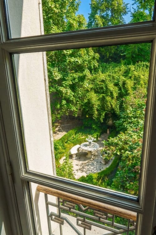 Vista del jardín desde la Chambre 2 del Château en Villa Raspail, Ivry-sur-Seine, con exuberante vegetación y fuente de piedra