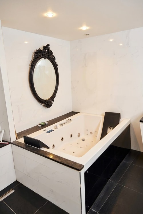 Lujosa bañera de hidromasaje con espejo negro ornamentado en el dormitorio de Villa Raspail, Ivry-sur-Seine
