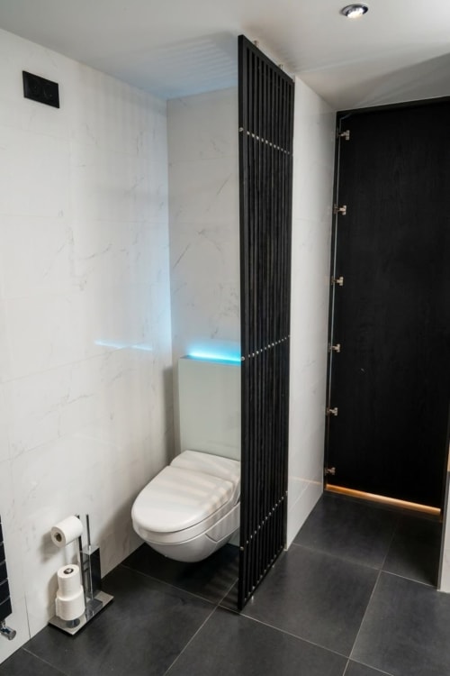 Baño moderno en Villa Raspail con inodoro mural, divisoria negra, iluminación azul ambiental y azulejos efecto mármol