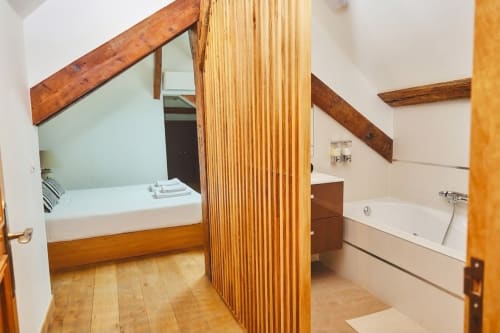 Dormitorio y baño ensuite de la Villa Raspail con vigas de madera, cama y bañera en Ivry-sur-Seine