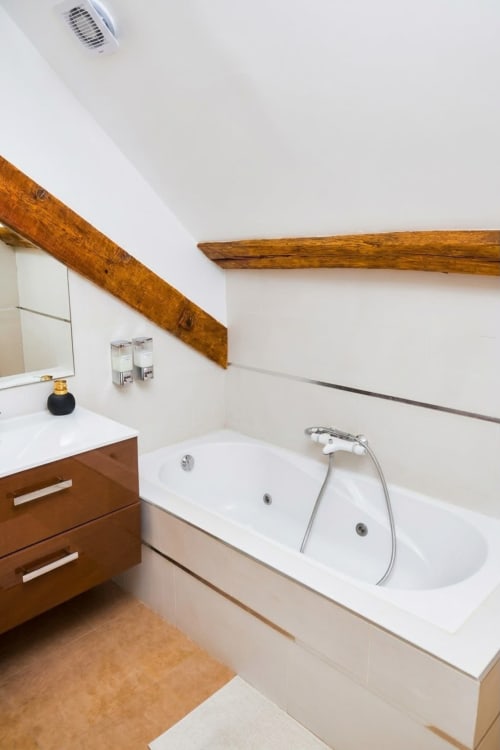 Baño moderno en Villa Raspail con vigas de madera, bañera blanca con chorros, vanidad de madera y sistema de ventilación