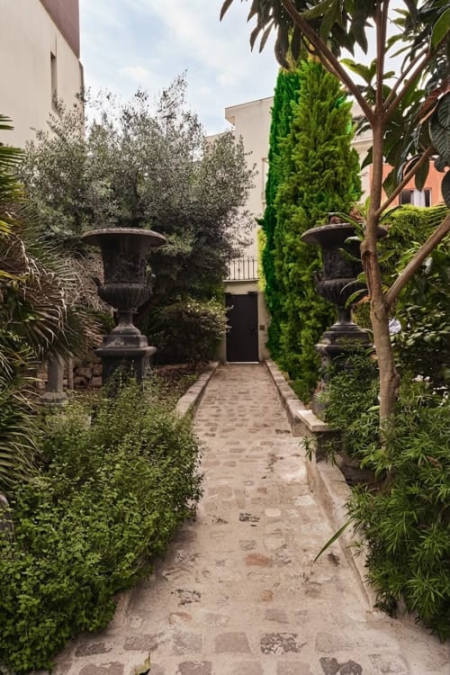 Elegante sendero del jardín en Villa Raspail en Ivry-sur-Seine con setos podados, urnas clásicas y frondosa vegetación