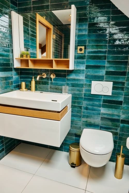 Baño moderno en Villa Raspail con azulejos color turquesa, lavabo blanco, accesorios dorados e inodoro montado en pared