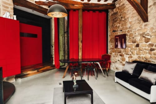 Espace de vie moderne à Villa Raspail avec murs rouges, chaises de salle à manger rouge et noir, foyer en pierre et