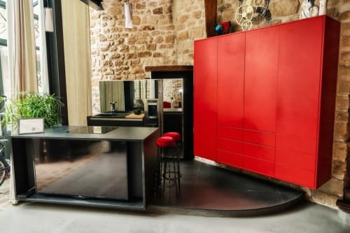 Espacio de vida moderna en Villa Raspail con armario rojo, escritorio negro, televisión y paredes de piedra vista en apartamento de Ivry-sur-Seine.