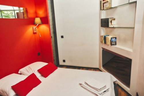 Dormitorio moderno en Villa Raspail Ivry-sur-Seine con pared de acento rojo, cama blanca, almohadas rojas, lámpara de pared y estanterías empotradas