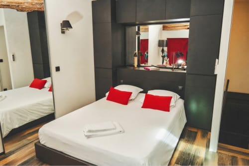 Dormitorio moderno en Villa Raspail con cama blanca, almohadas rojas, mobiliario oscuro, espejo y piso de madera en Ivry-sur-Seine