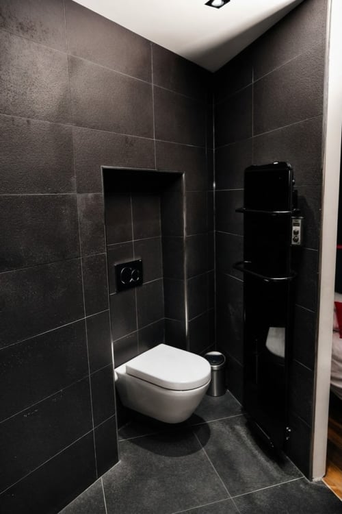 Baño moderno en Villa Raspail Ivry con azulejos negros, inodoro blanco montado en pared y accesorios de acero inoxidable