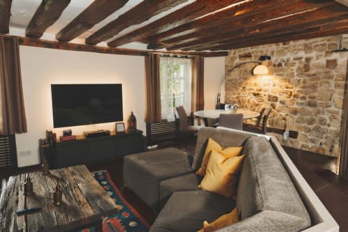 Salón moderno con vigas vistas, muros de piedra, sofá gris, televisor y zona de comedor en Villa Raspail, Ivry-sur-Seine