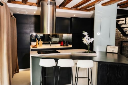 Cocina moderna con gabinetes negros, campana de acero inoxidable, taburetes blancos y vigas de madera en Villa Raspail