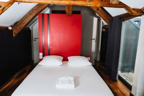 Dormitorio moderno en Villa Raspail con pared acentuada en rojo, vigas de madera expuestas, ropa de cama blanca y comodidades contemporáneas