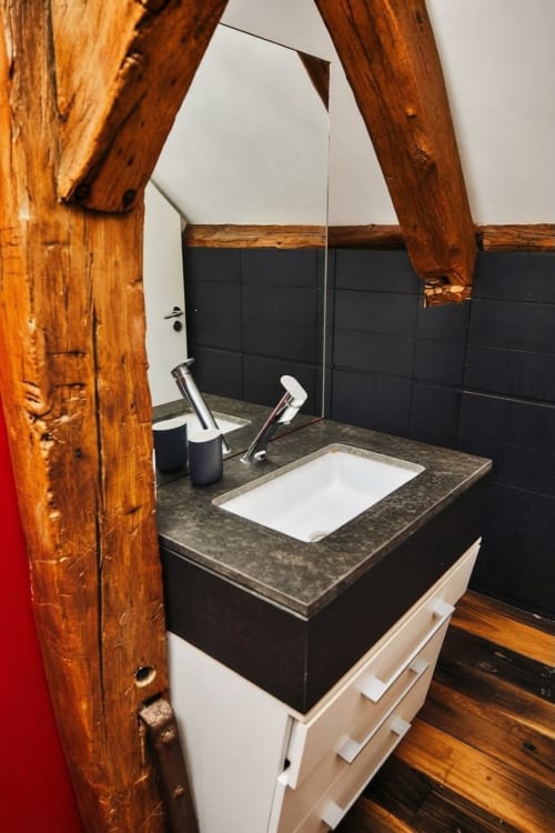 Baño moderno con paredes de azulejos oscuros, lavamanos con encimera oscura, vigas de madera rústica y espejo en el apartamento Villa Raspail