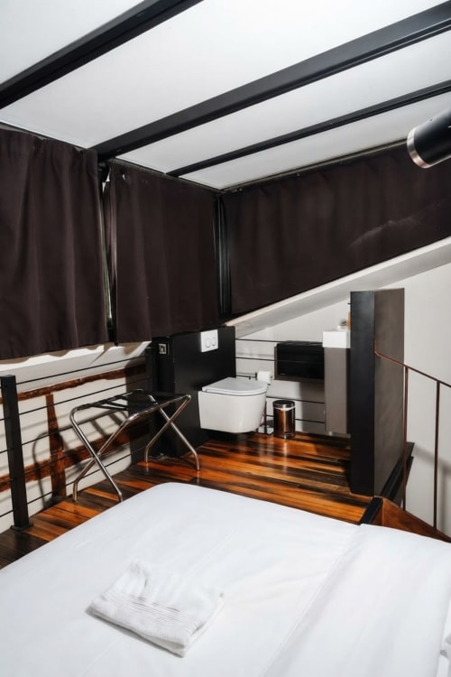 Dormitorio loft moderno con baño privado en Villa Raspail, Ivry-sur-Seine, claraboya, cortinas oscuras, elementos de madera