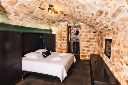 Dormitorio moderno en el apartamento de piedra de Villa Raspail con cama blanca, accesorios oscuros y techo rústico en Ivry sur Seine
