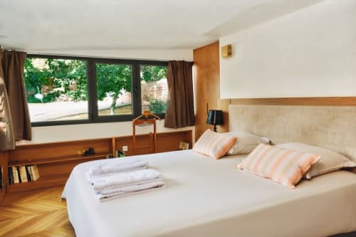 Dormitorio luminoso en Villa Raspail con vista al jardín, muebles de madera, almohadas a rayas y amplias ventanas