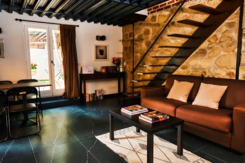 Dormitorio de estilo loft moderno en Villa Raspail con sofá naranja, escalera negra, muros de piedra y acceso al jardín