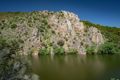 Acantilados rocosos de piedra caliza con vegetación verde sobre las tranquilas aguas del río en La Machacona, España