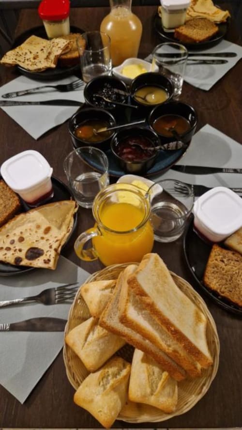 Petit-déjeuner Le Perroquet Bleu : pain grillé, pâtisseries, jus d'orange, confitures et tartinades sur table foncée