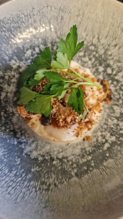 Mise en bouche gourmande du Perroquet Bleu : base onctueuse, garniture croustillante et persil frais sur assiette texturée